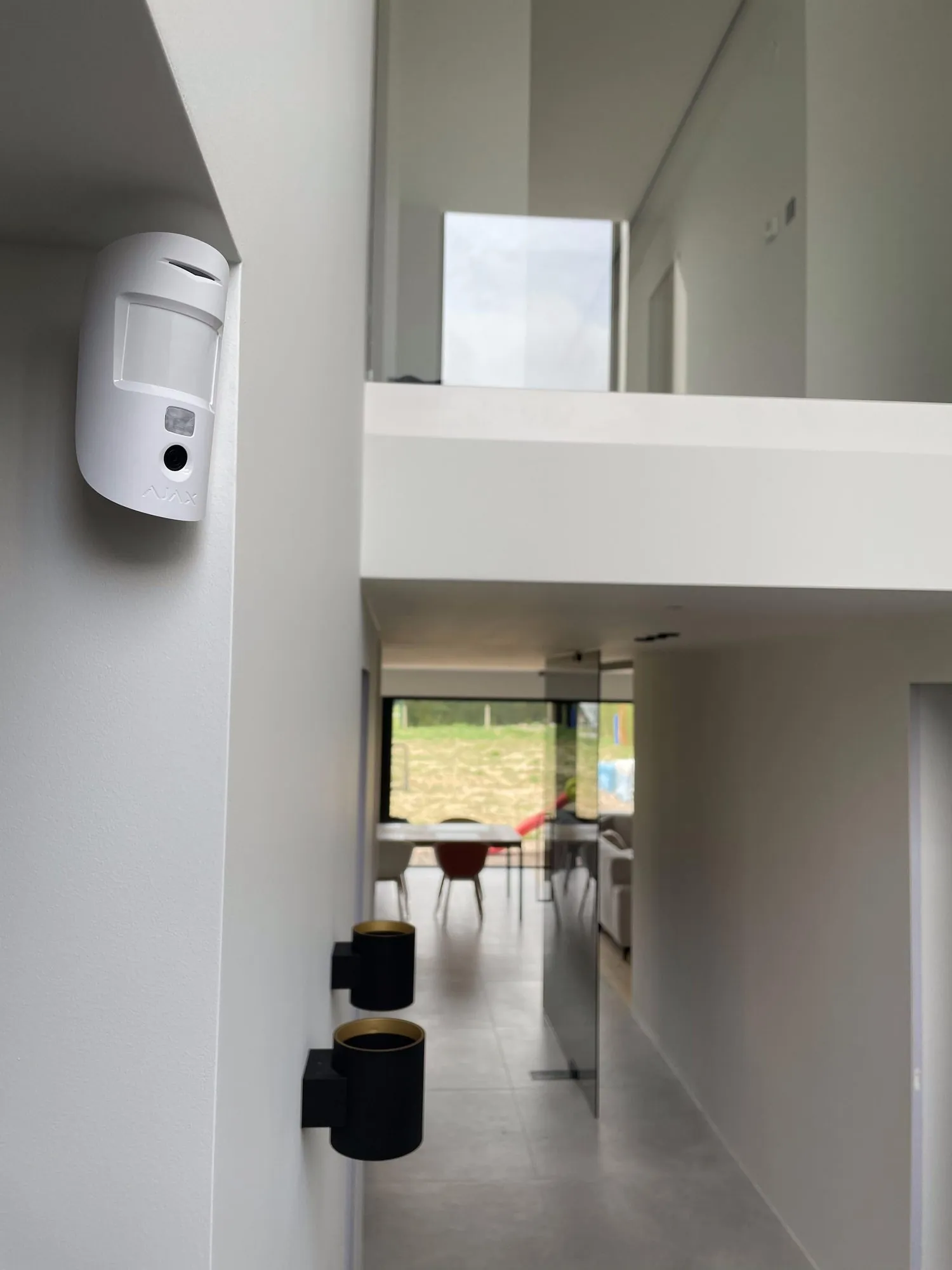 Witte bewegingsmelder aan muur in moderne gang met open zicht op woonkamer
