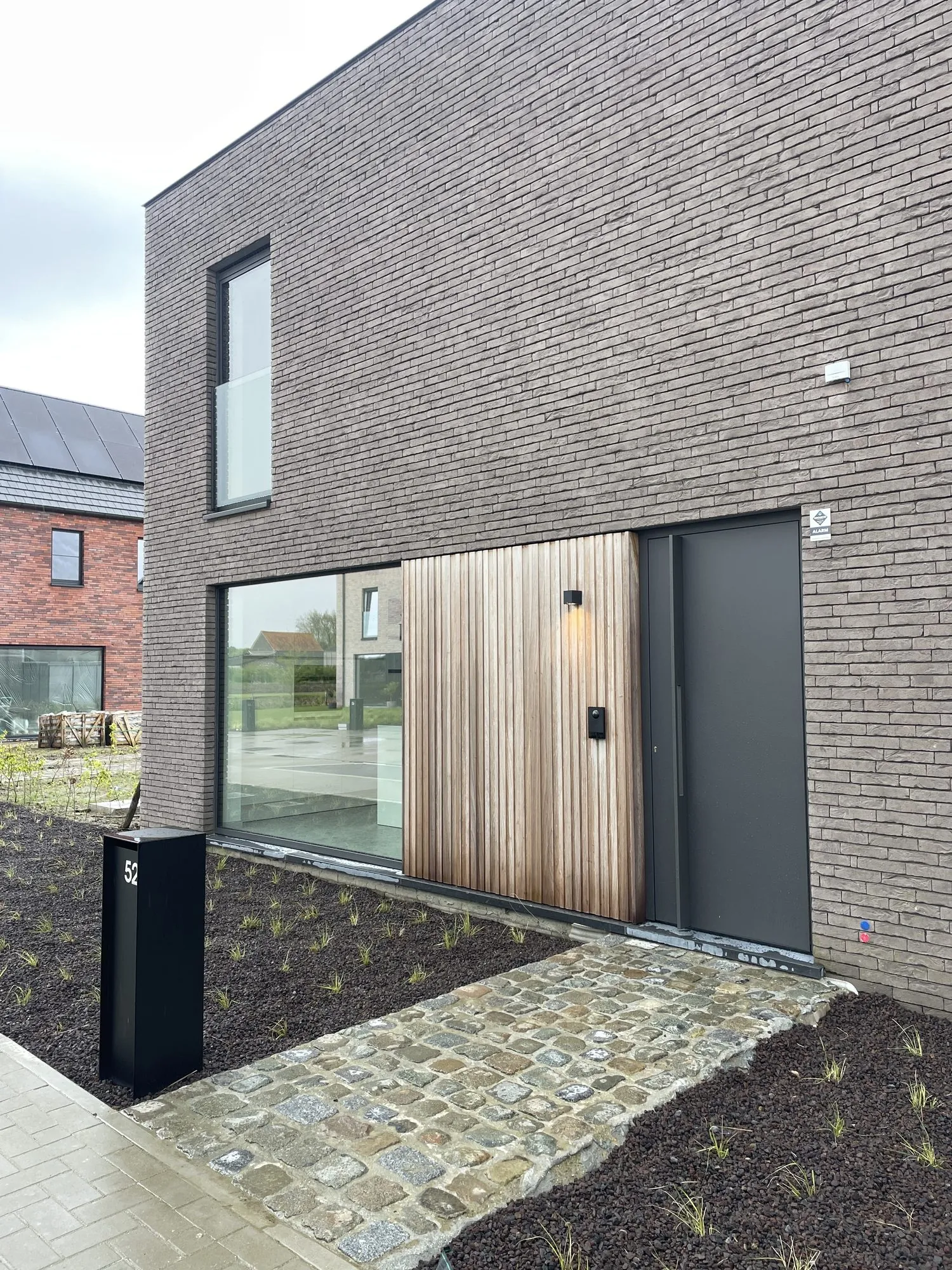 Moderne bakstenen woning met grote ramen, toegangsdeur en camerabewaking aan de gevel