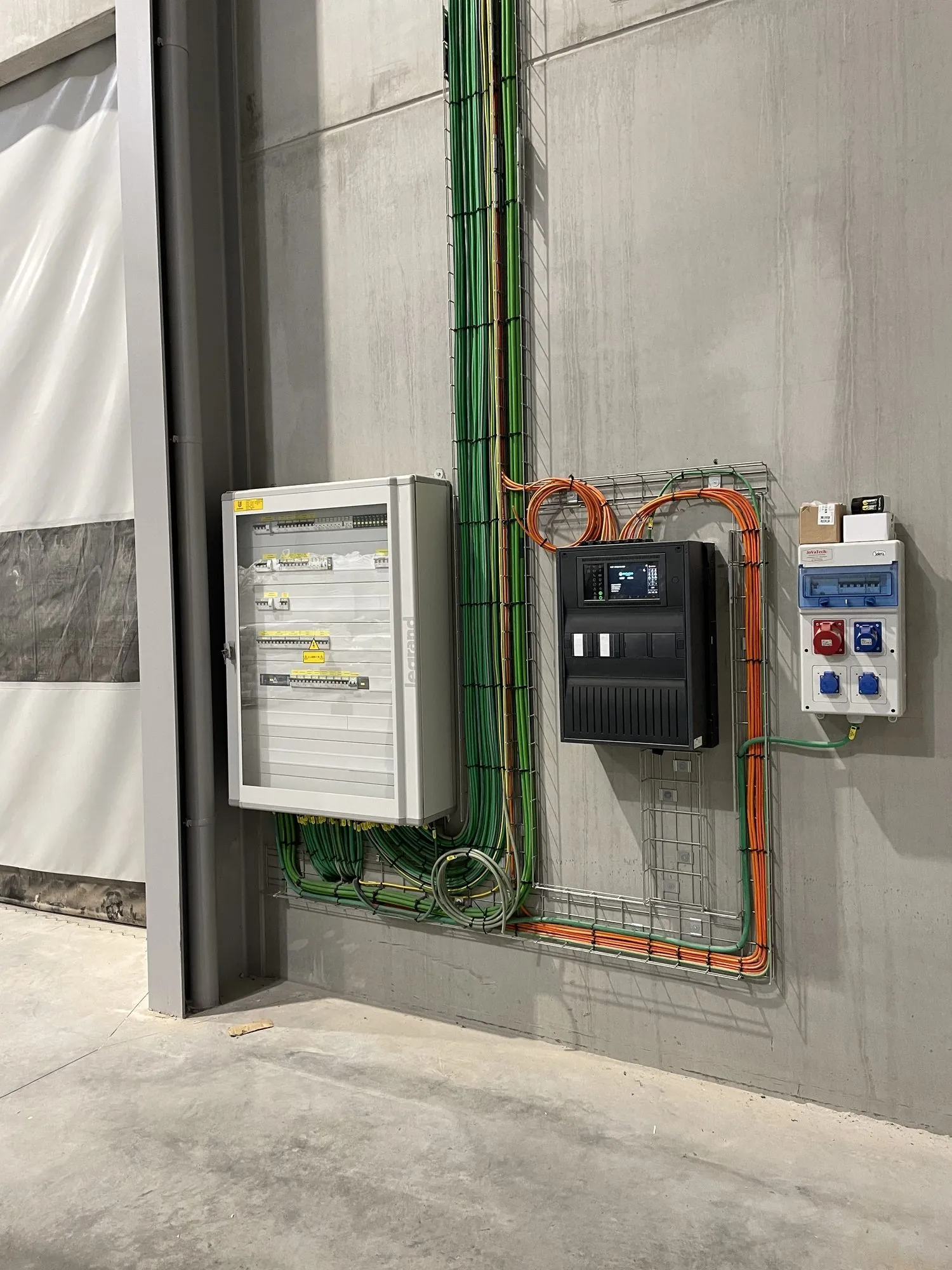 Professionele elektrische installatiekast met zekeringen, besturingselementen en groen-oranje kabels tegen betonnen wand