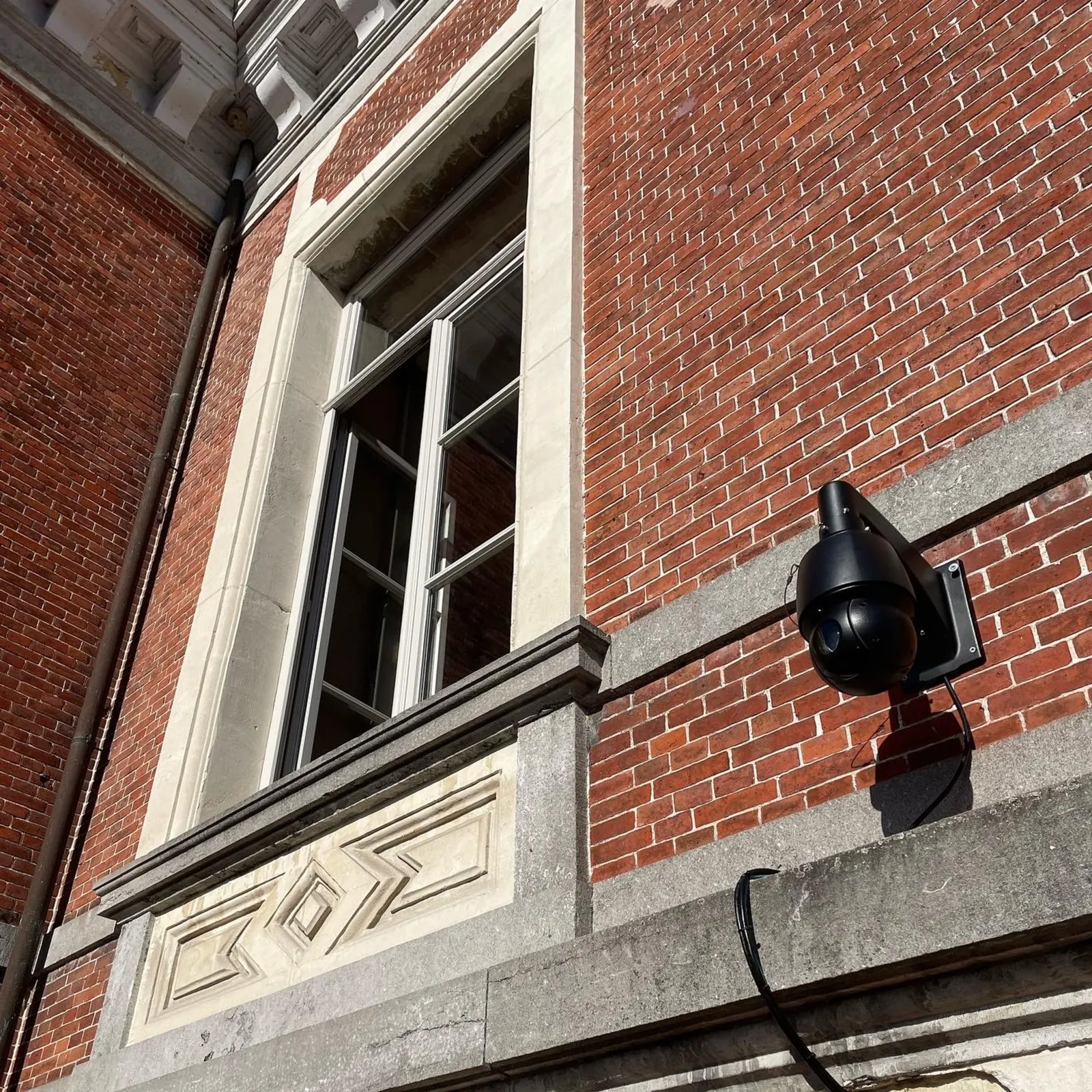 Zwarte beveiligingscamera bevestigd op een bakstenen muur naast een raam van een gebouw