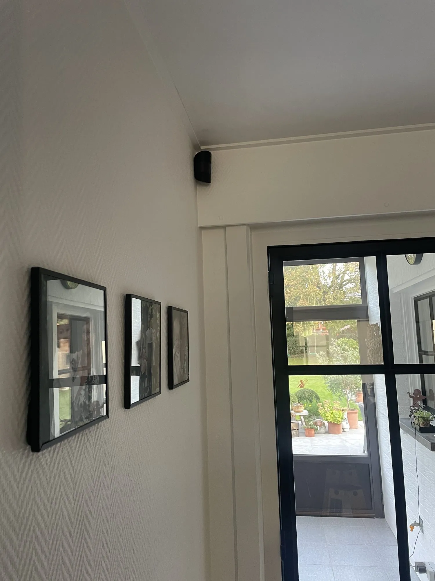 Bewegingsmelder gemonteerd aan plafond bij deur, naast spiegels aan muur in interieur