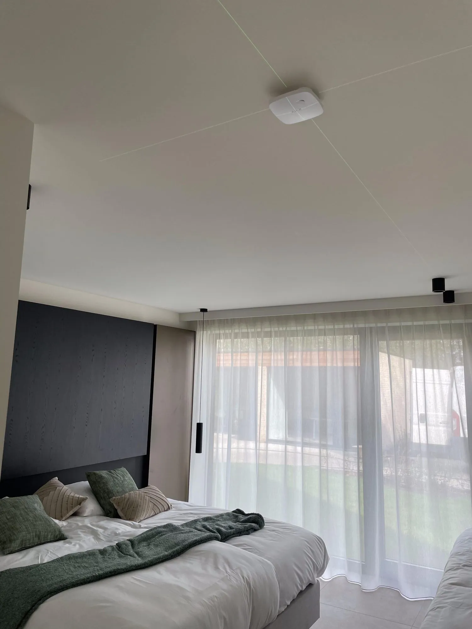 Rauchmelder an het plafond van een slaapkamer met bed en ramen met gordijnen