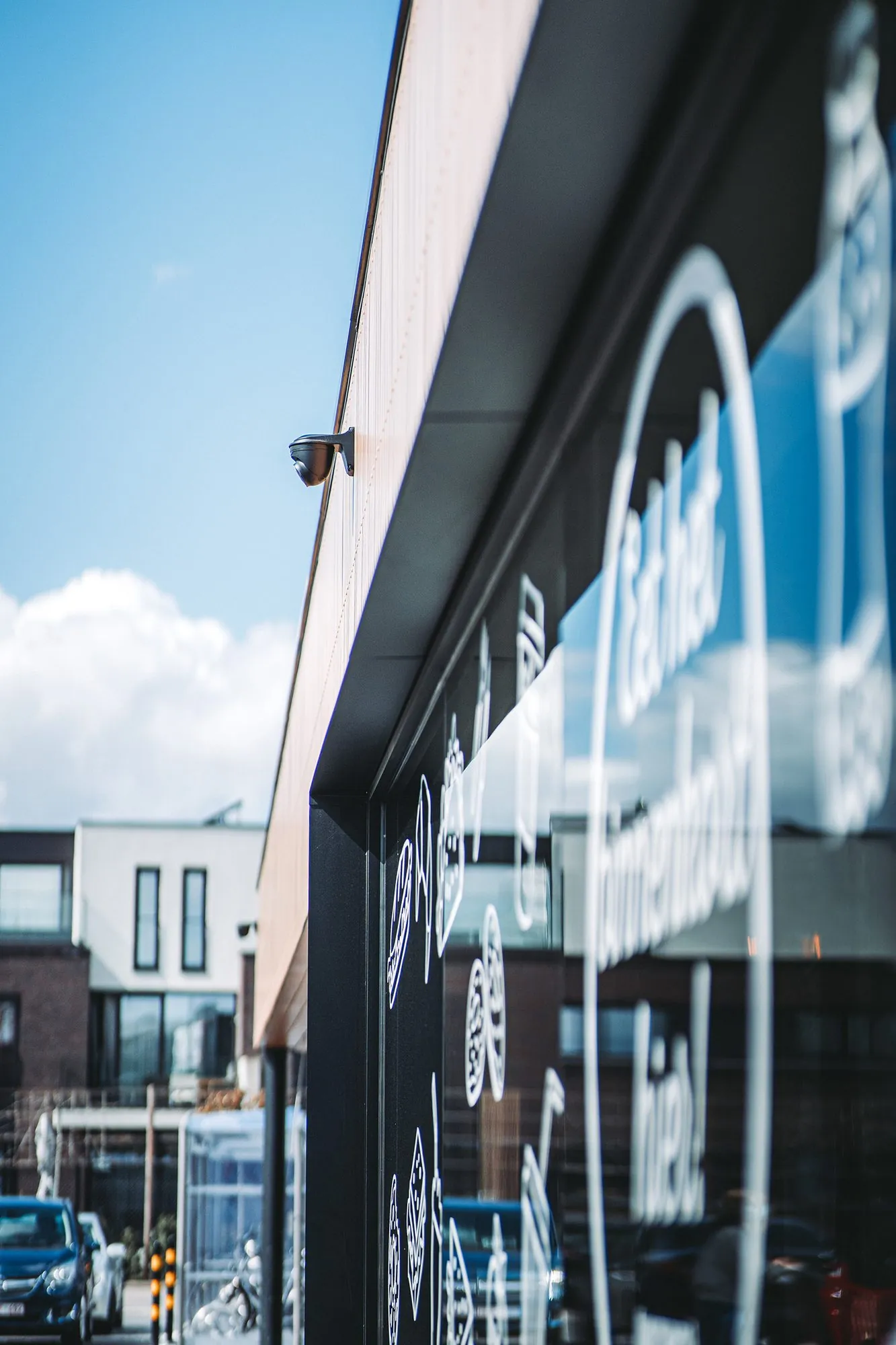 Beveiligingscamera op de gevel van een modern bedrijfsgebouw met parkeerplaatsen en andere gebouwen op de achtergrond