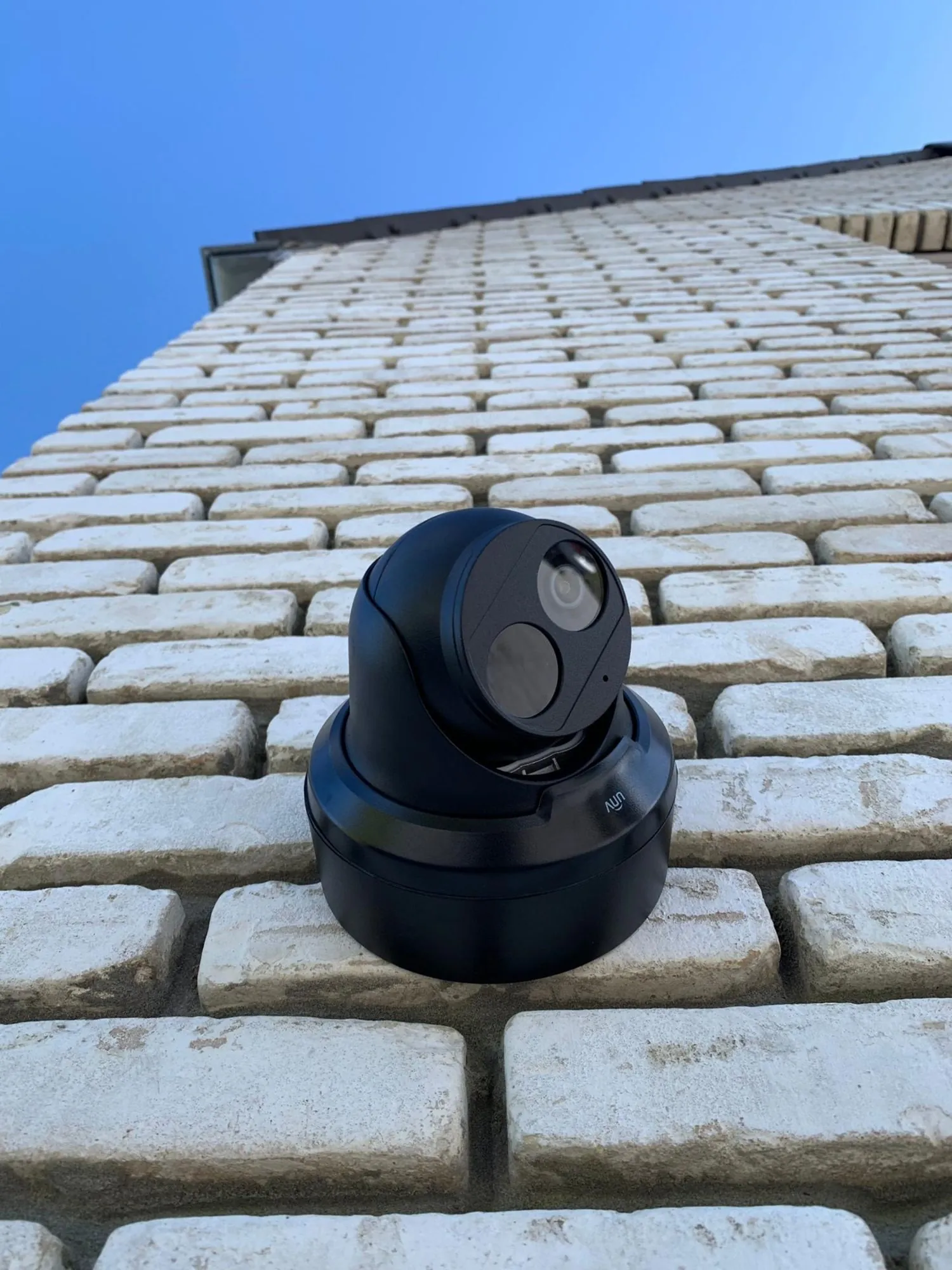Zwarte dome camera met dual lens gemonteerd op een witte bakstenen muur onder blauwe hemel