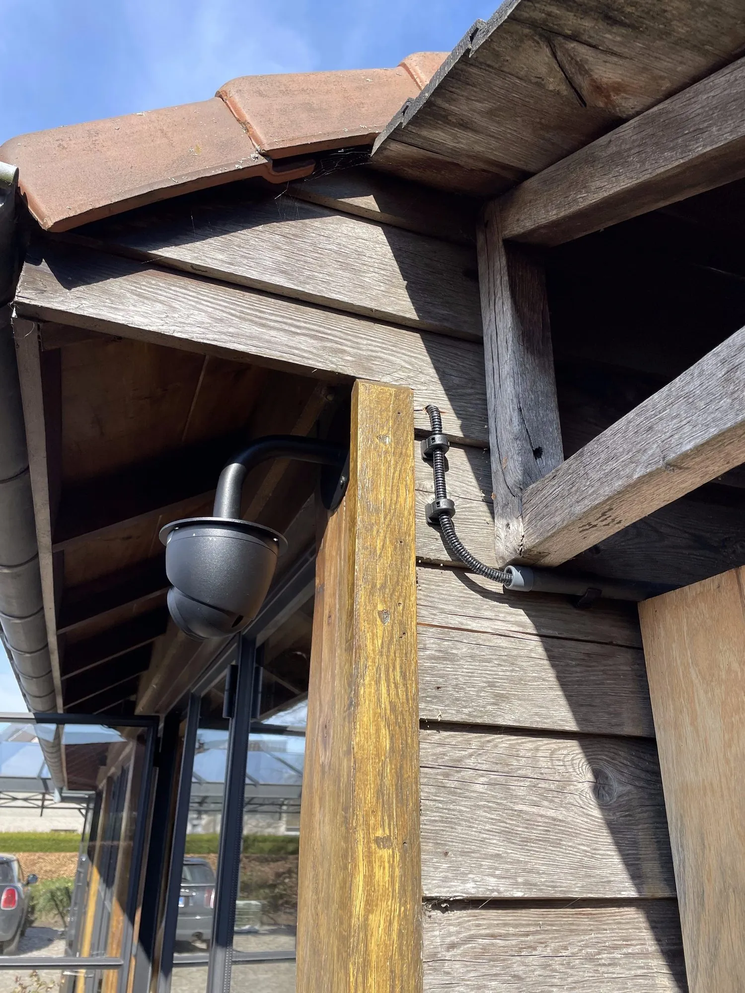 Zwarte koepelcamera bevestigd onder het houten dak van een bedrijfsgebouw met zichtbare bedrading