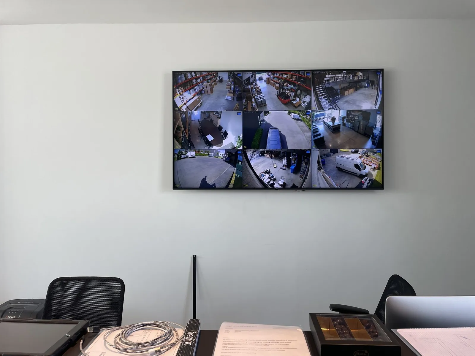 Wandgemonteerde monitor toont live camerafeed van zes verschillende ruimten in een bedrijfspand