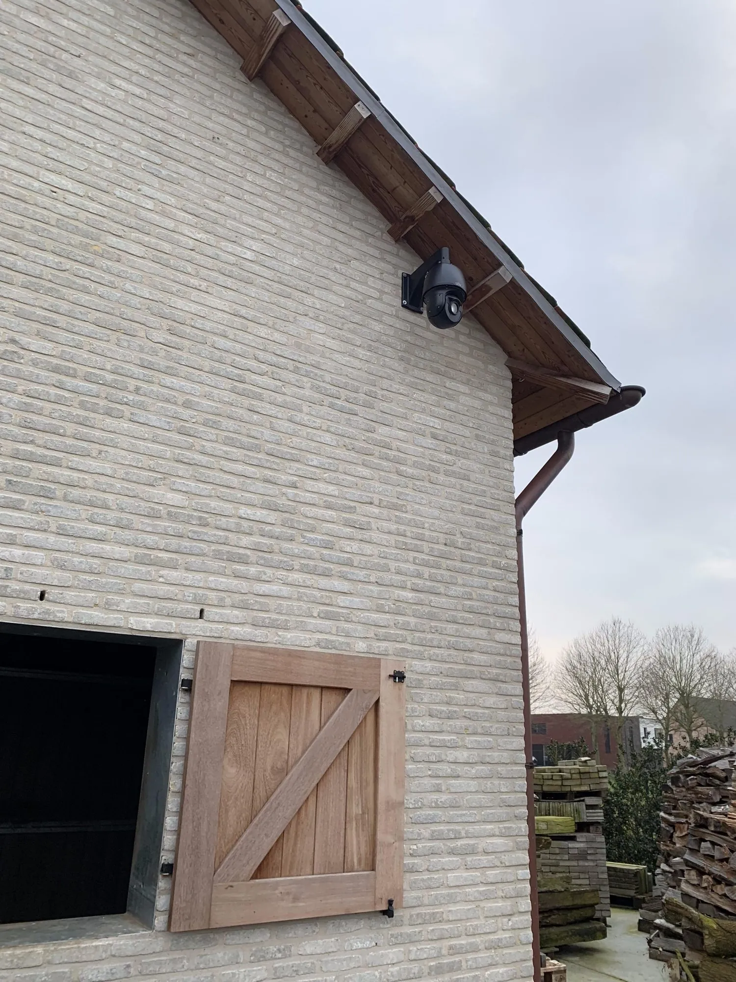 Zwarte camera met PTZ-functie bevestigd aan de bakstenen gevel van een woning, gericht op de ingang