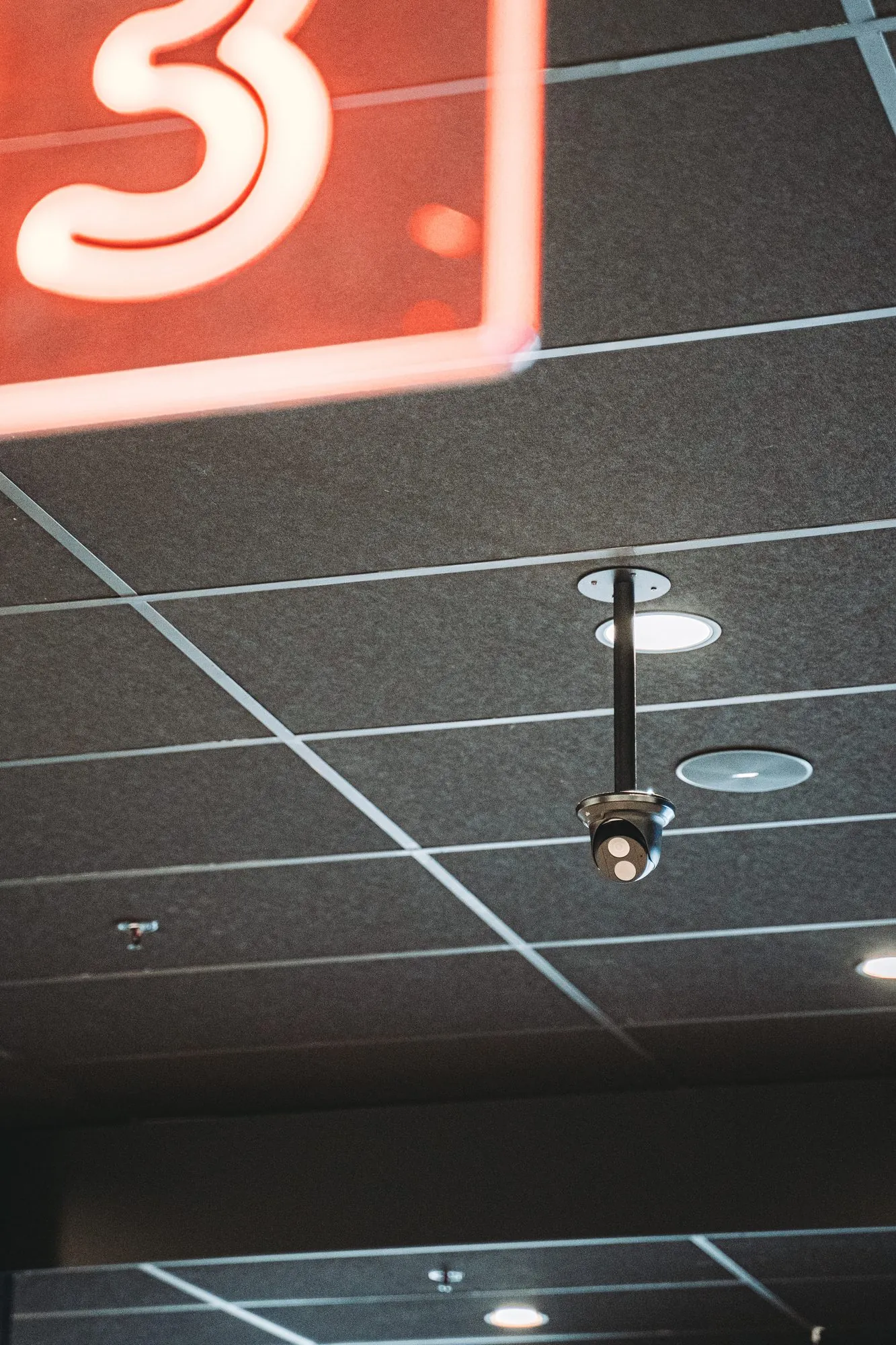 Beveiligingscamera bevestigd aan een plafond met neonrood bord op de achtergrond in een modern interieur