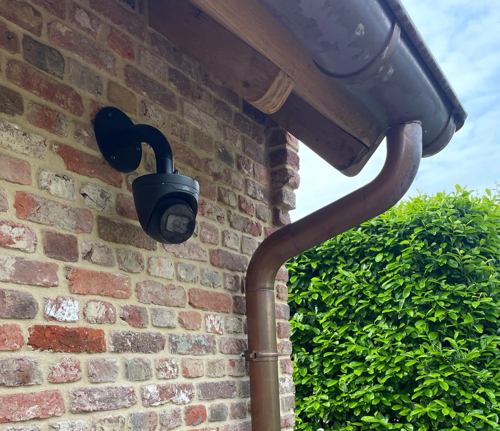 Zwarte beveiligingscamera gemonteerd op een bakstenen muur, gericht op de voorgevel van een woning