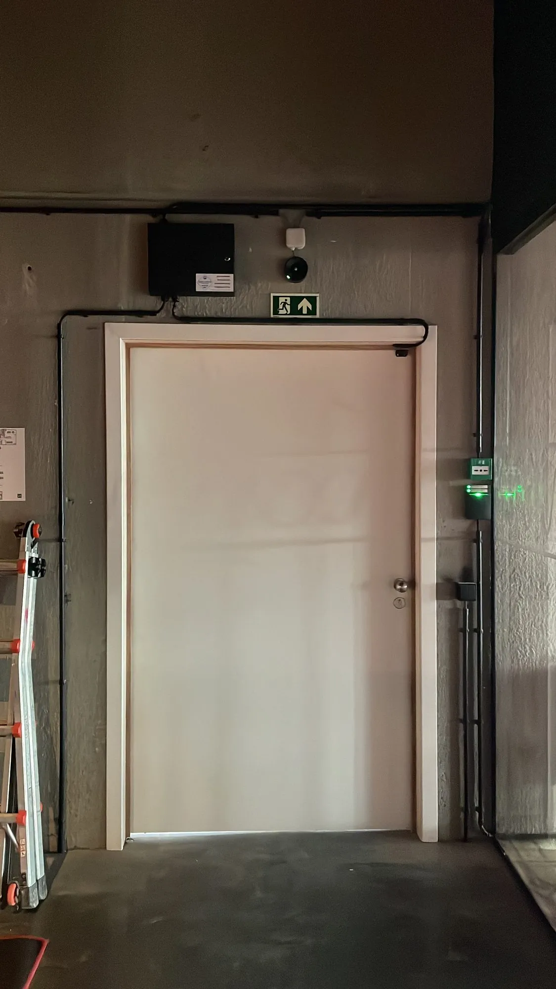 Toegangscontrole aan deuropener met groen verlichte toegangskaartlezer en nooduitgangsbordje boven de deur