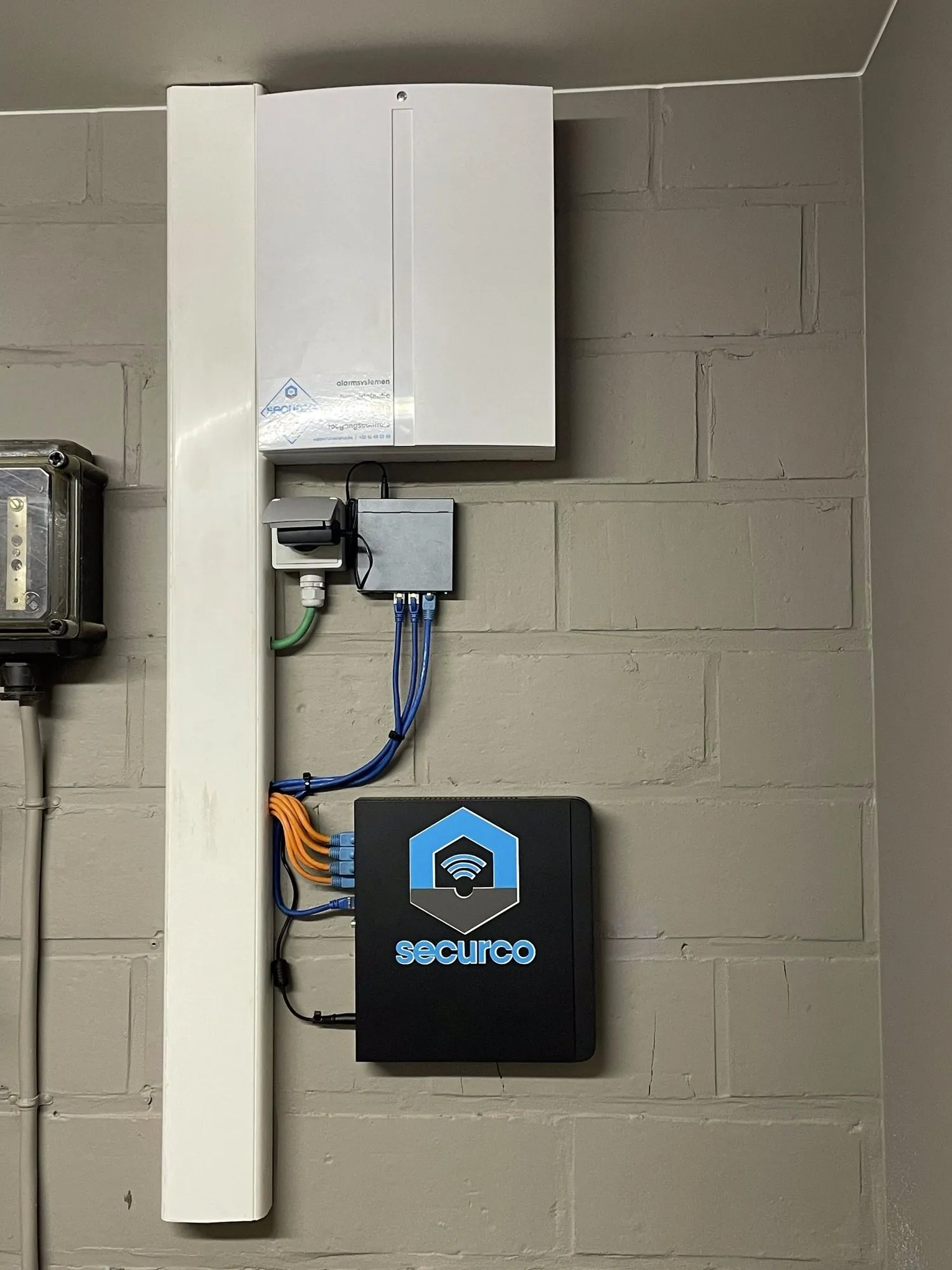 Installatie van een SecurCo beveiligingssysteem aan de muur met witte centrale unit, aansluitingen en zwarte bedieningskast