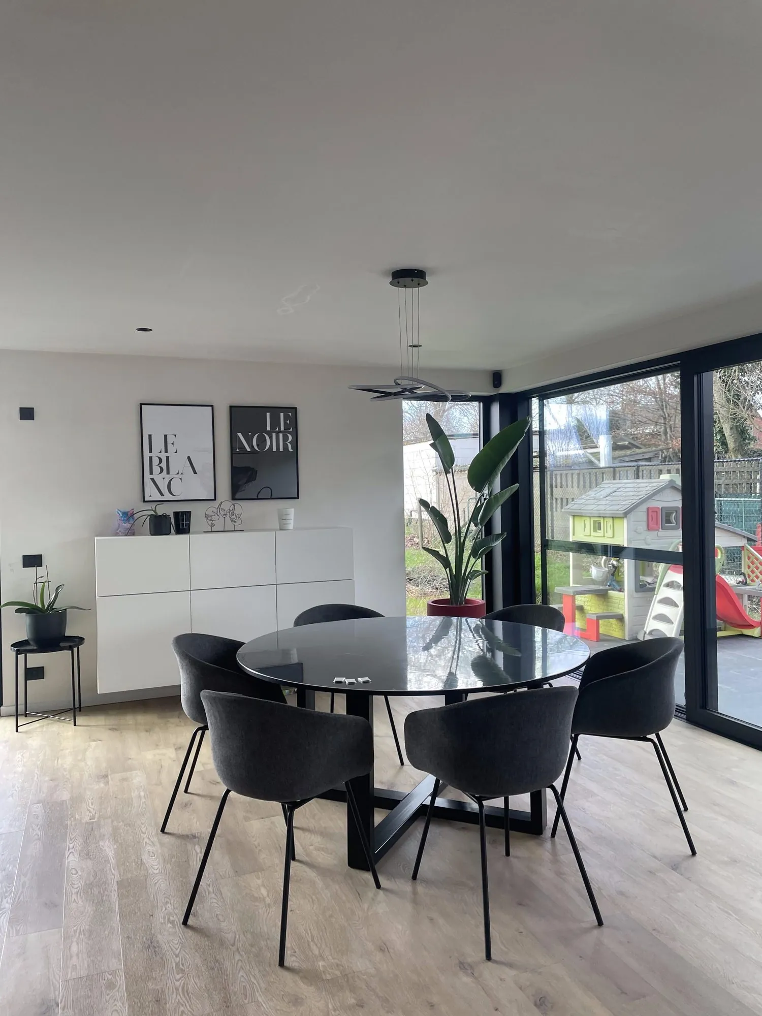 Modern woonkamer met ronde zwarte tafel, zwarte stoelen en grote glasschuifdeuren met uitzicht op terras