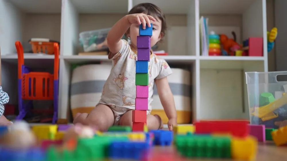 Klein kind bouwt een toren van gekleurde blokken in een veilige speelruimte met opbergsystemen