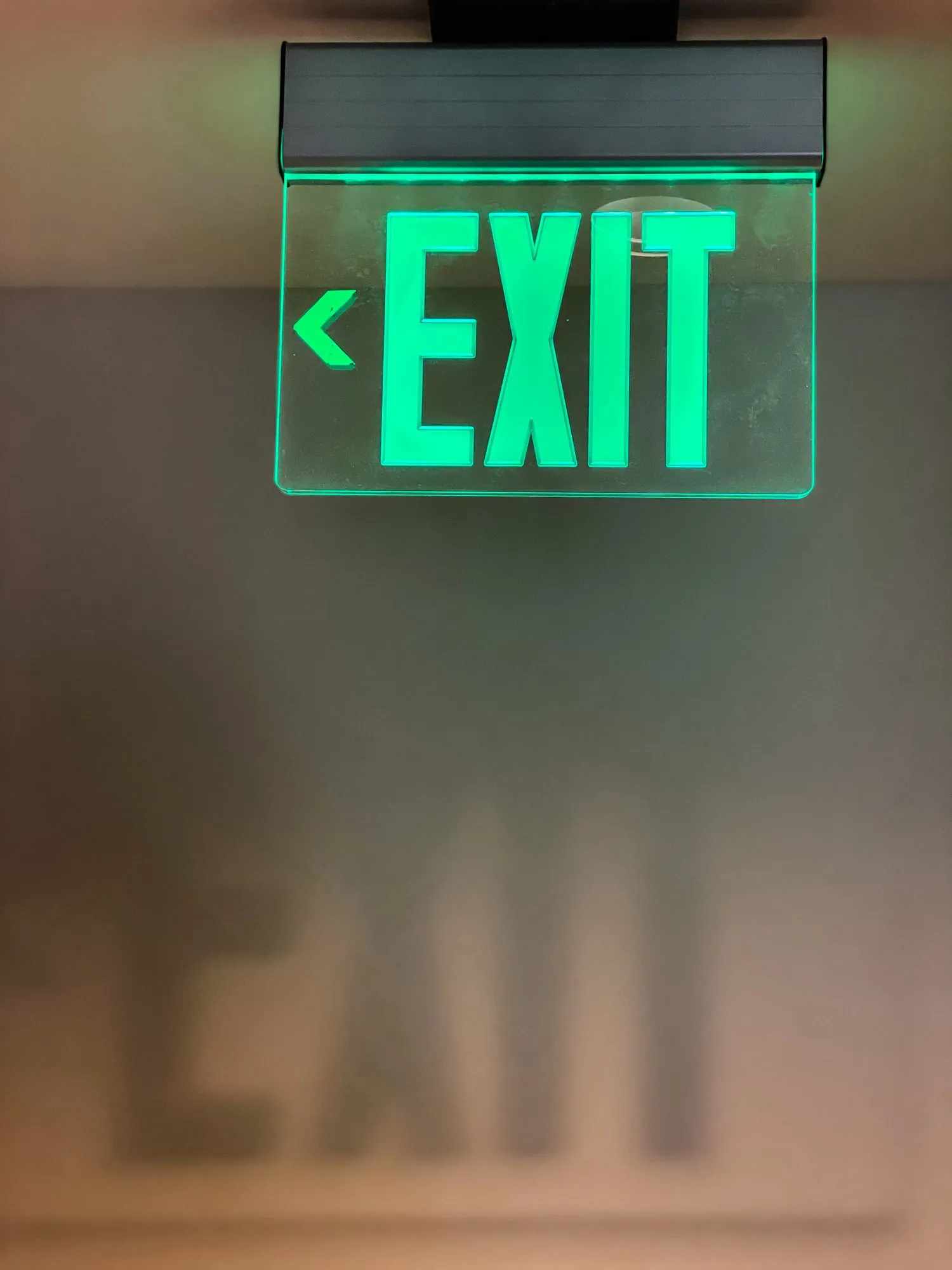 Groen neonbord met EXIT-tekst en pijl naar links, hangend aan plafond