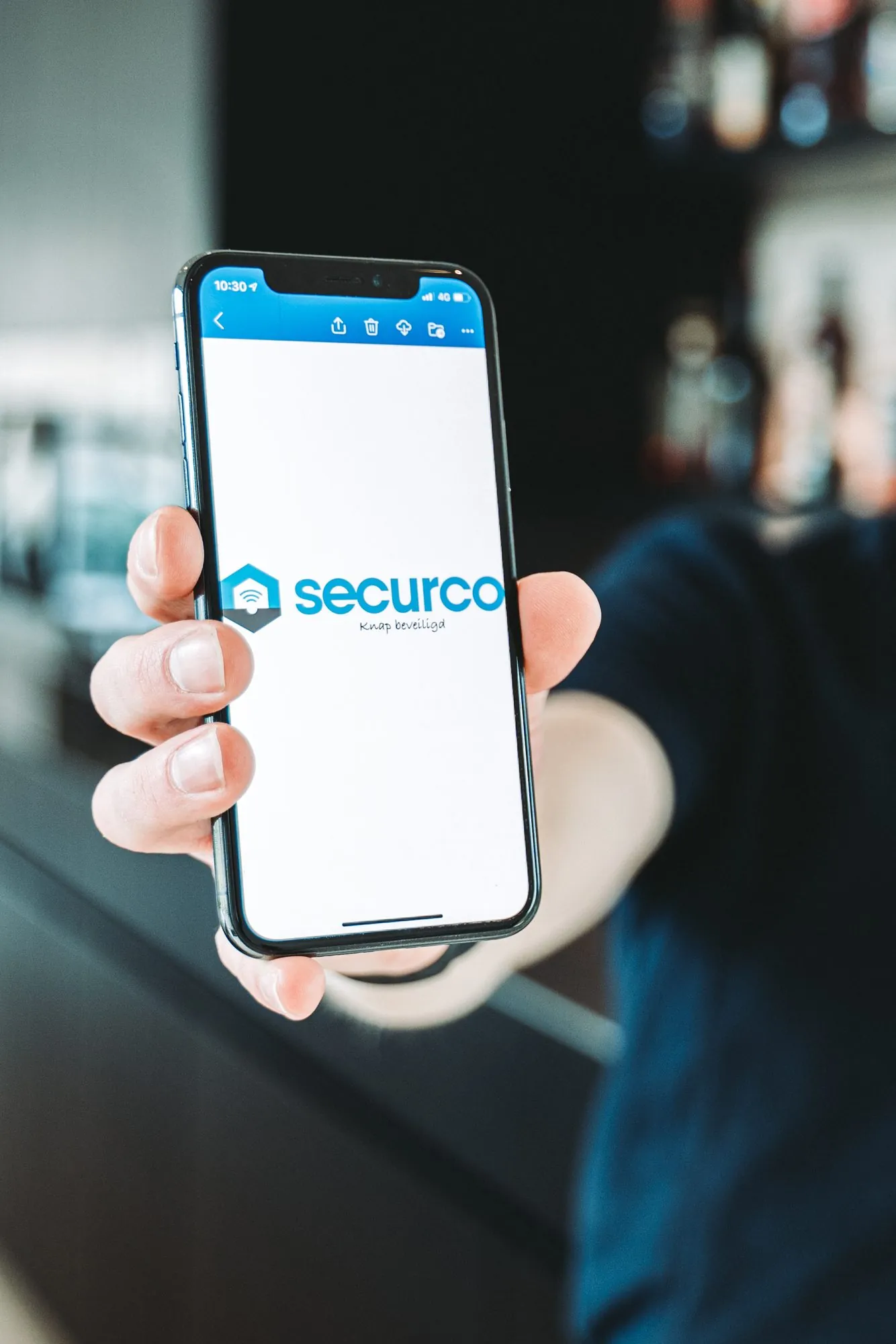 Smartphone waarop de SecurCo app is geopend met het logo en de tagline 'Klaar beveiligd' zichtbaar op het scherm