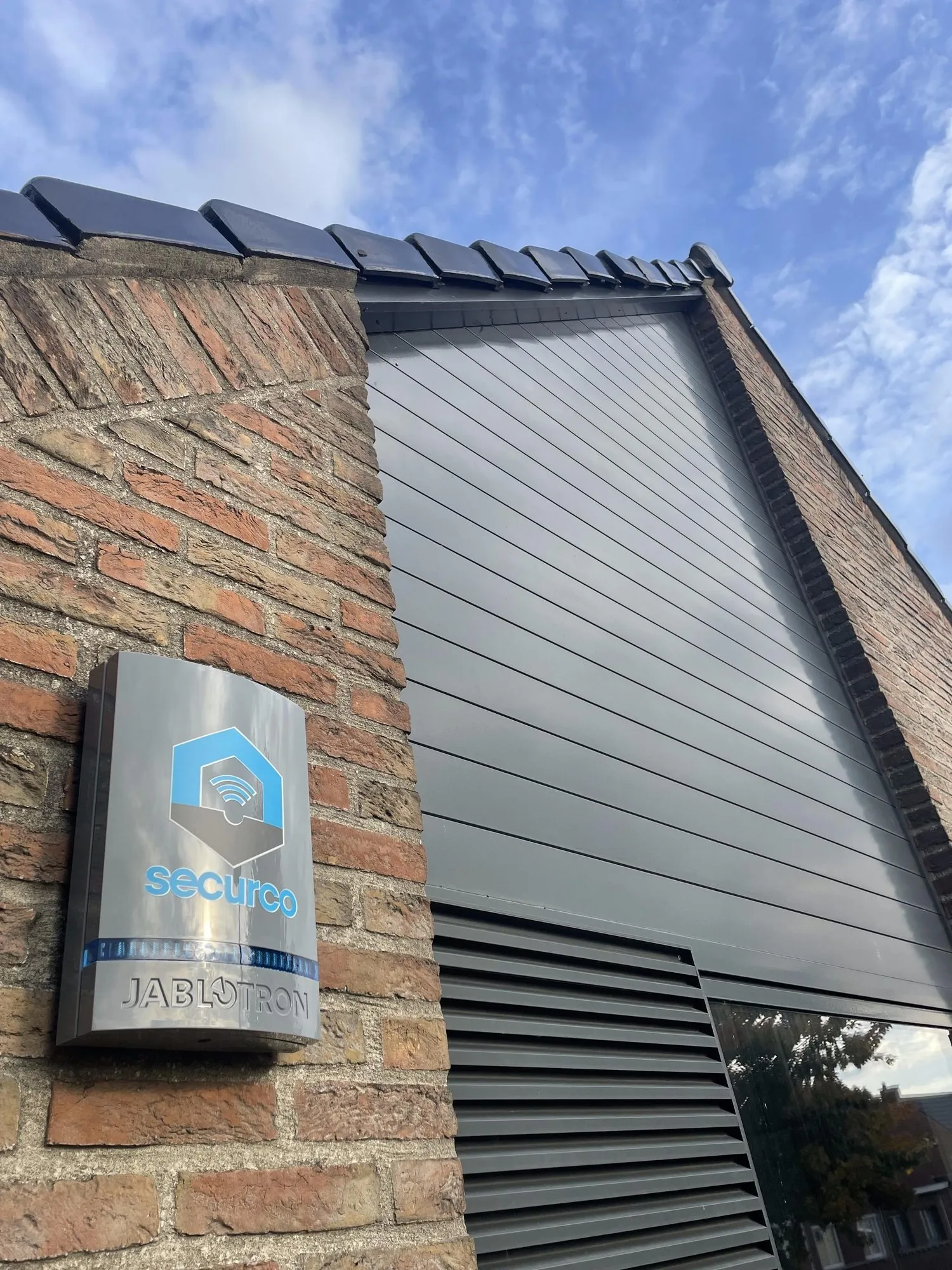 SecurCo-bordje op bakstenen muur met daarachter een moderne woning met zonnepanelen op het dak