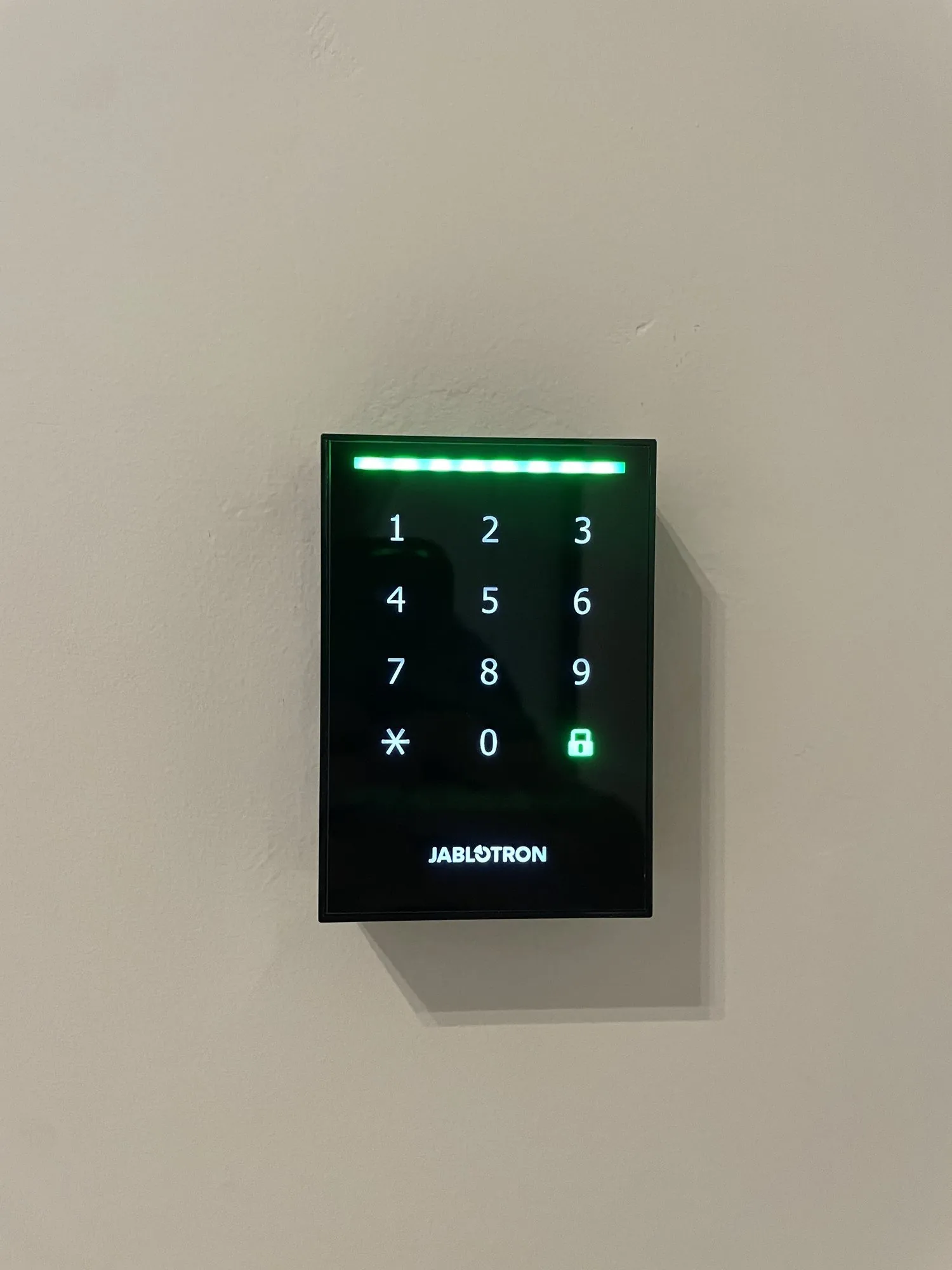 Jablotron toegangscontrolepaneel met verlicht numeriek toetsenbord en groen slotpictogram op witte muur